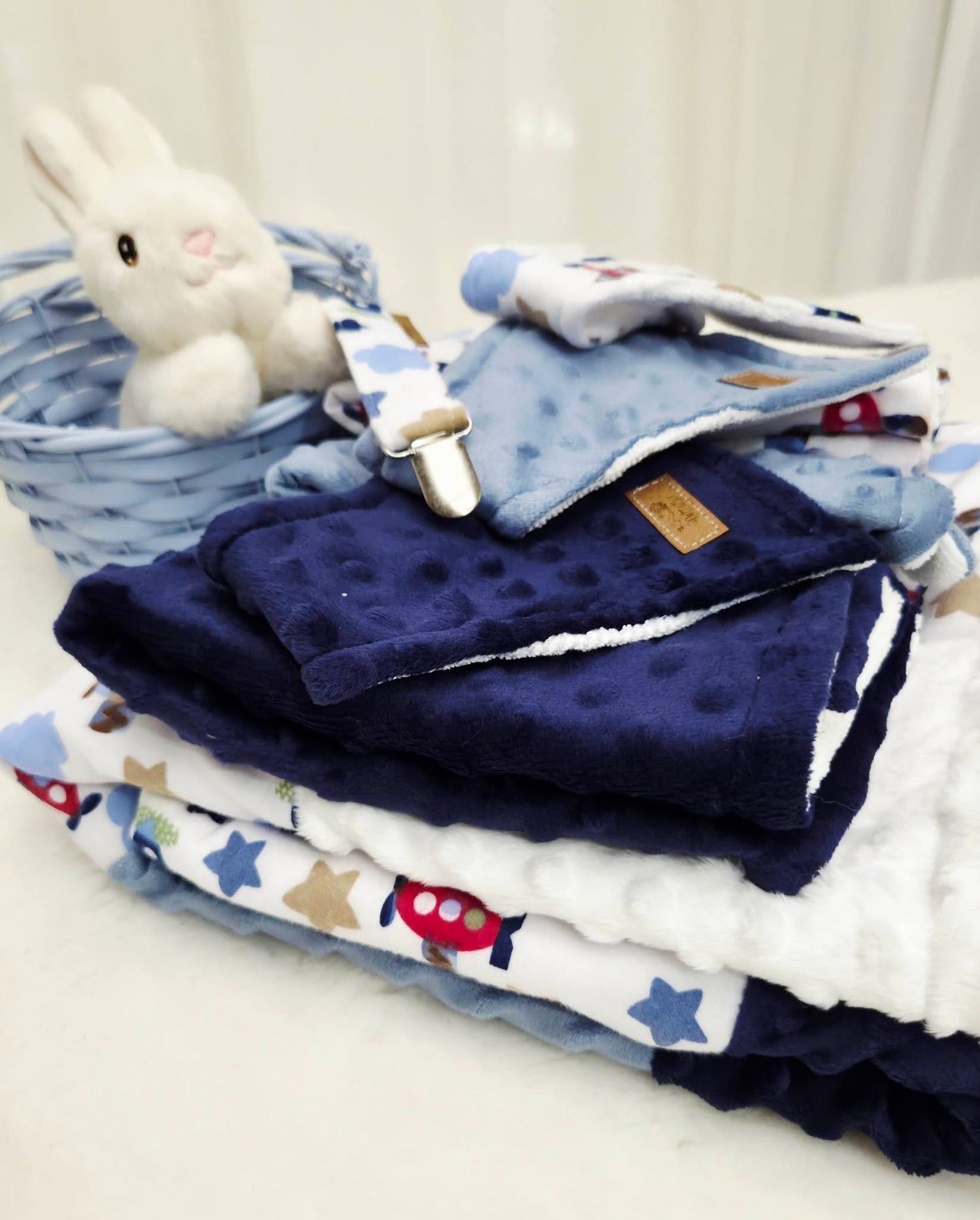 Blue baby blanket set with minky dot fabric, airplane print, pacifier clip, and white bunny plush toy in a wicker basket.