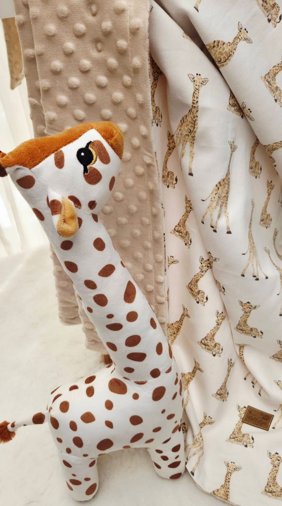Handmade giraffe stuffed animal toy beside a pink minky blanket with giraffe print pattern.