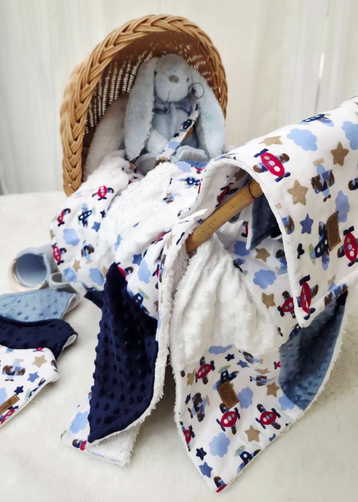 Baby blanket set with airplane print in blue, white, and red, displayed with a stuffed bunny in a wicker bassinet.