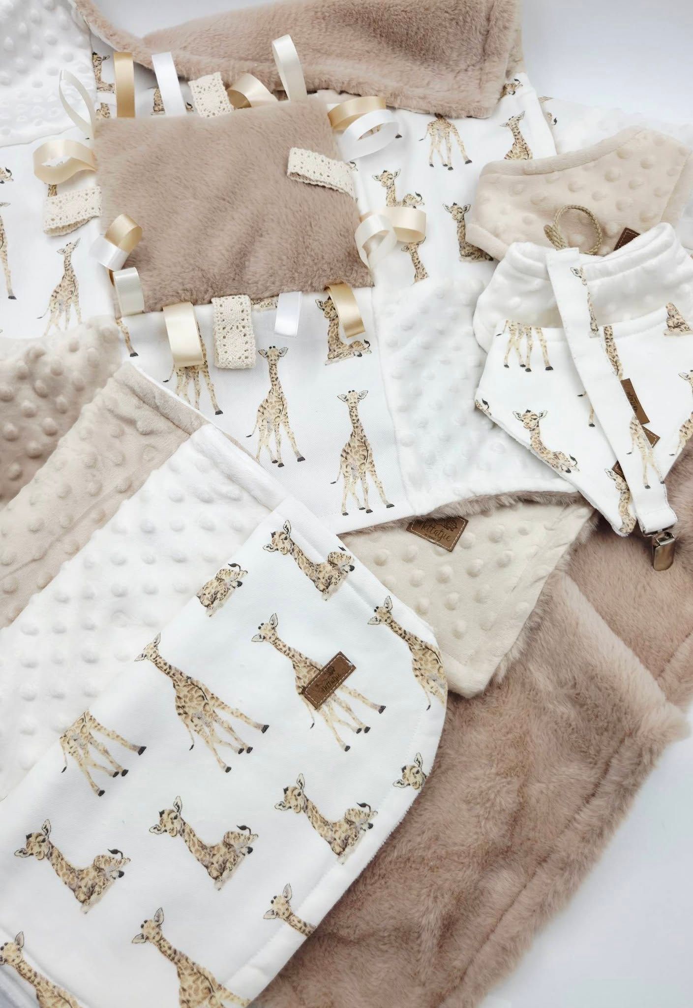 Neutral beige giraffe print baby gift set with minky blanket, taggie toy, and onesie on white background.