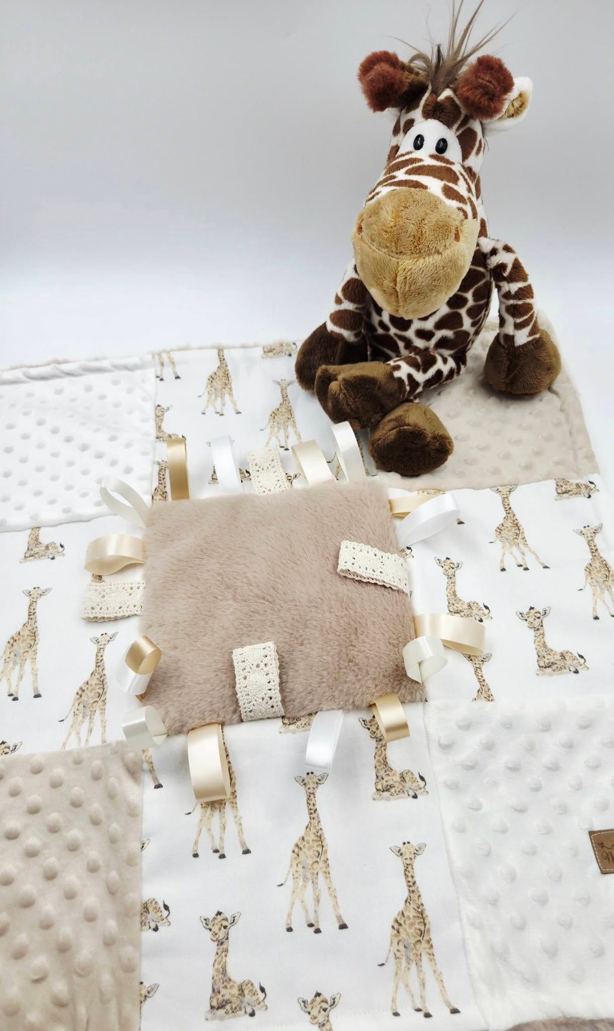 Giraffe-themed baby gift set with plush toy, minky blanket, and sensory taggie blanket in neutral beige tones.