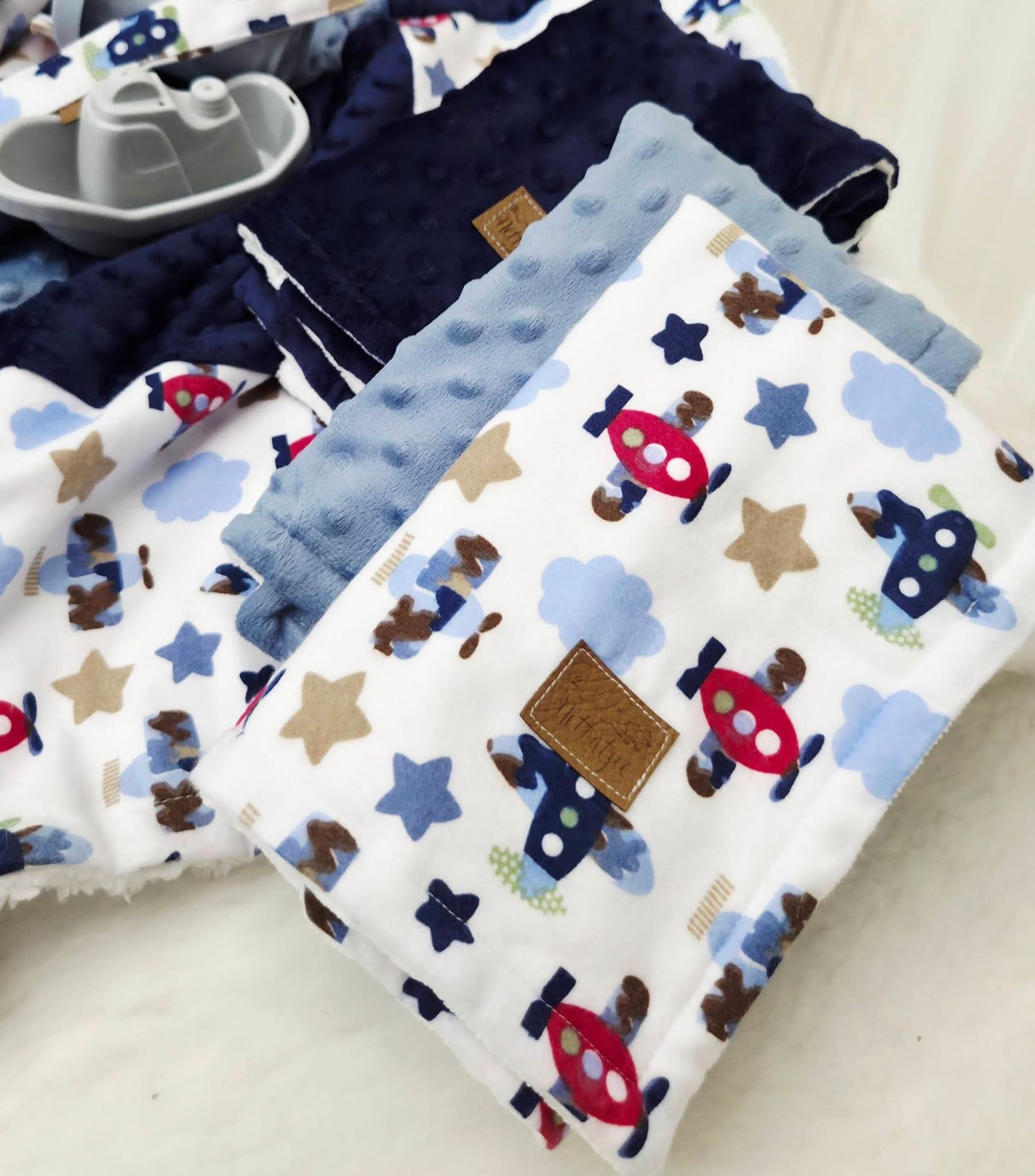 Baby blanket with airplane, star, and bear print in blue, red, and tan, with navy minky dot backing.