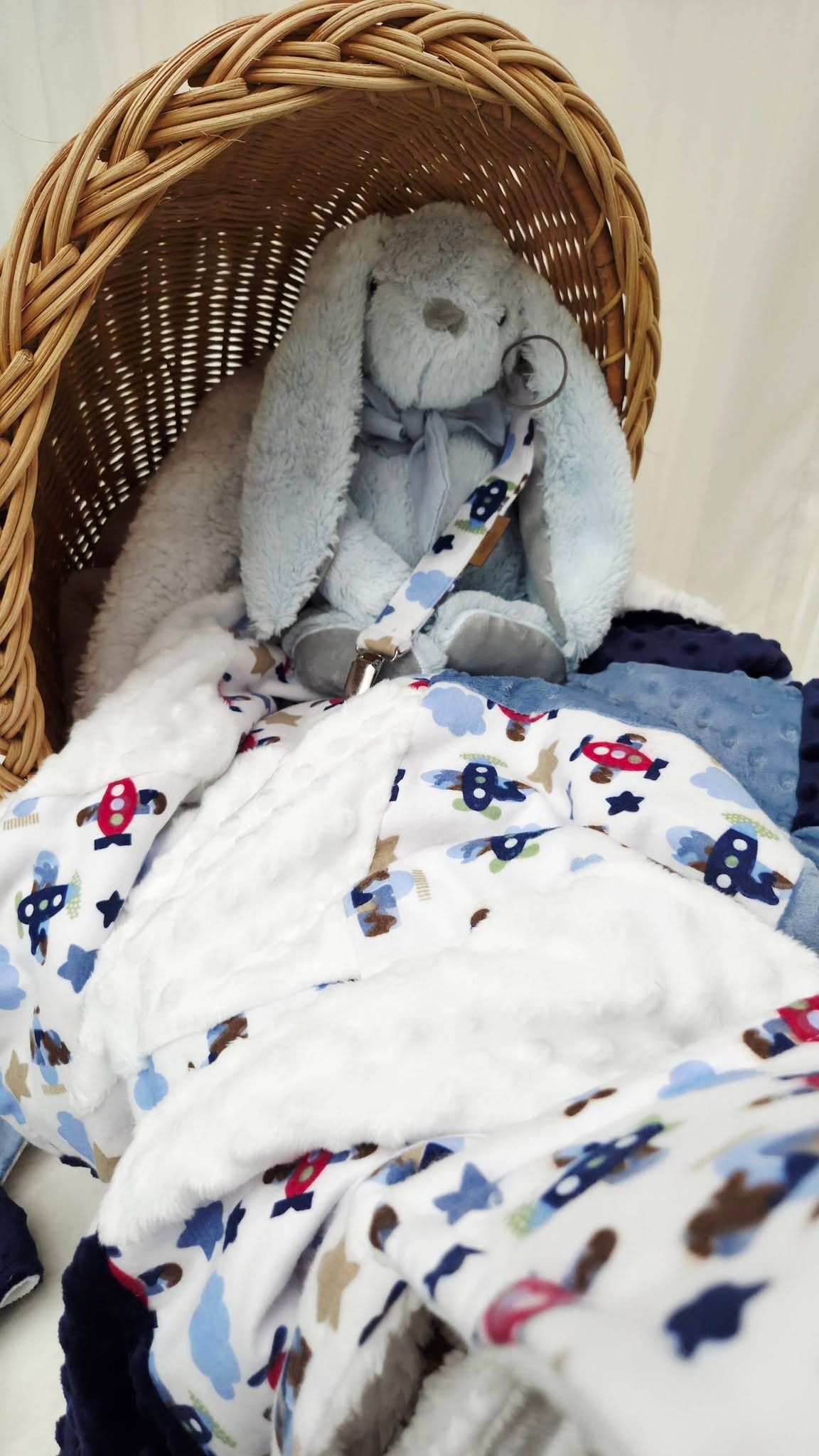 Wicker Moses basket with blue bunny plush toy and patterned baby blanket featuring airplanes and clouds.
