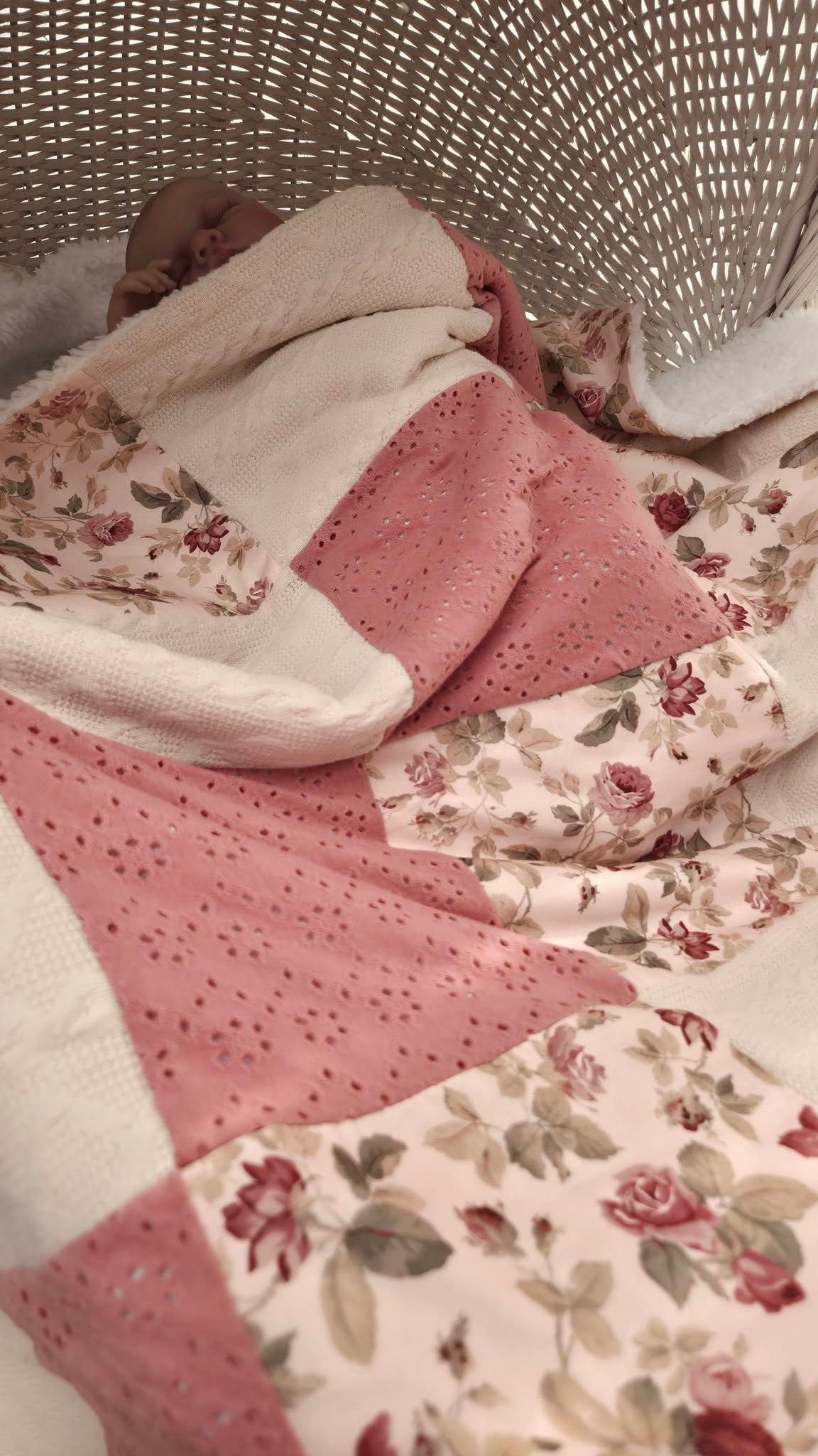 Pink floral patchwork quilt with eyelet fabric squares in a white wicker laundry basket.