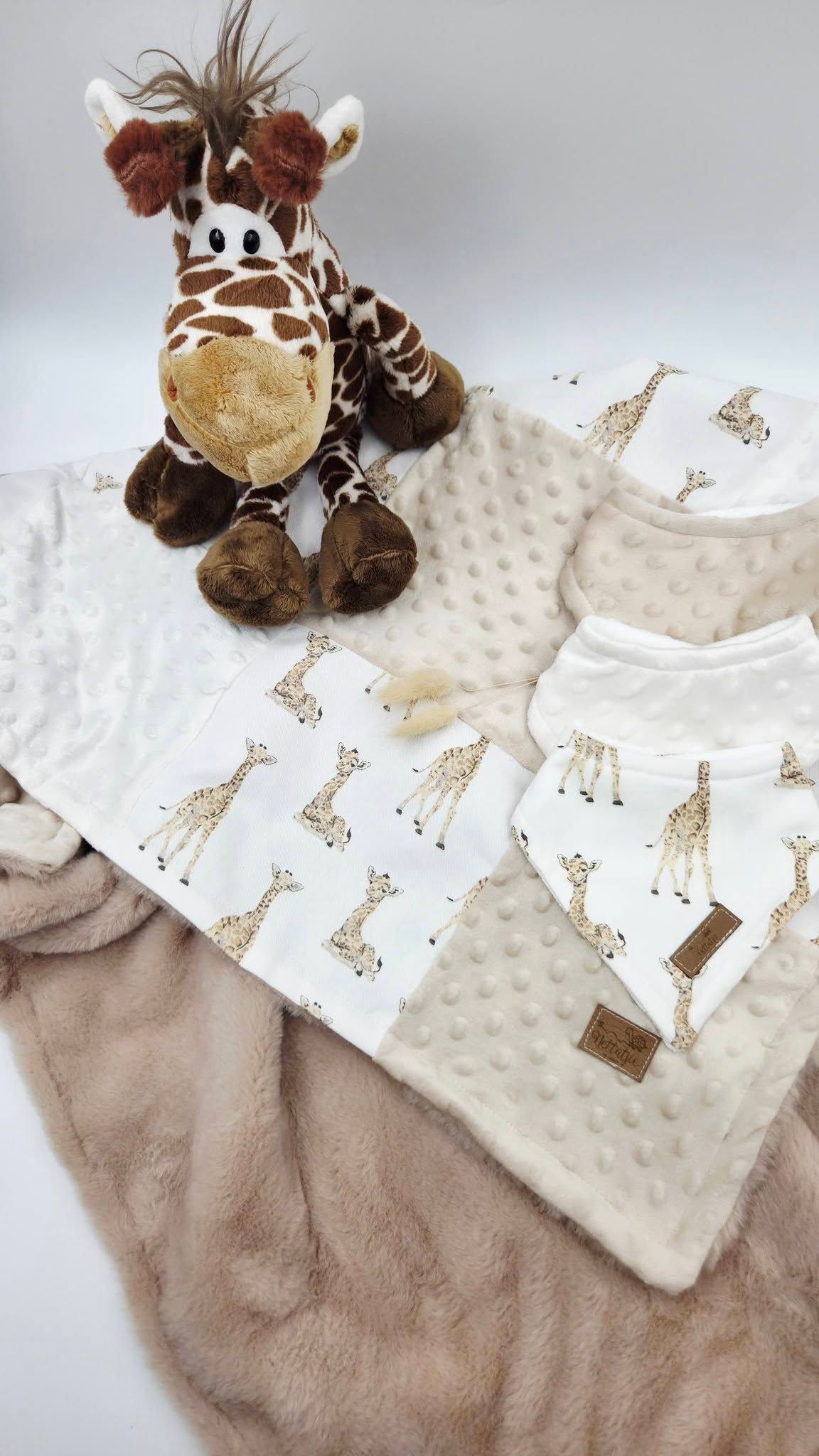 Giraffe-themed baby gift set with plush toy, minky blanket, bib, and burp cloth in neutral beige tones.
