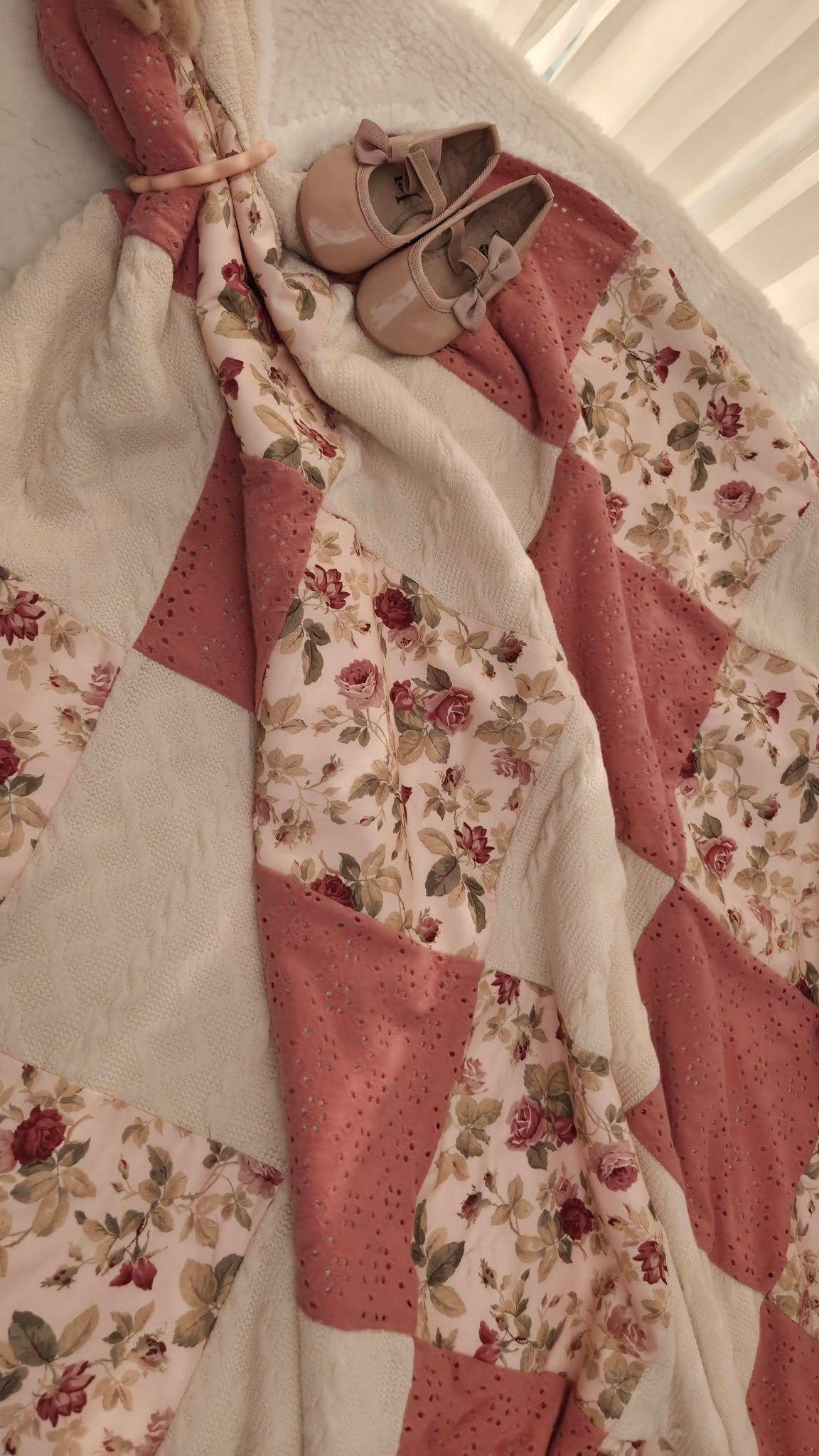 Pink floral patchwork quilt with rose pattern squares and tiny baby Mary Jane shoes, perfect for a nursery.