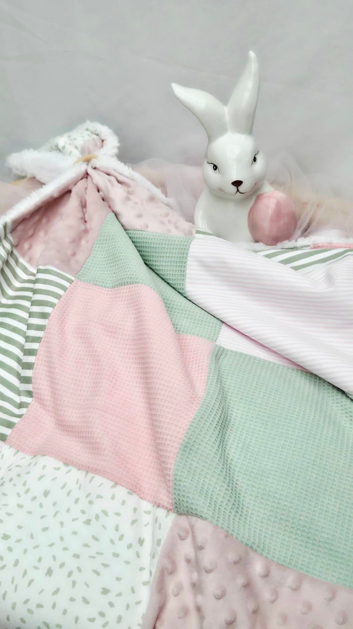 Pink and mint green patchwork baby quilt with ceramic white bunny figurine and plush lovey toy.
