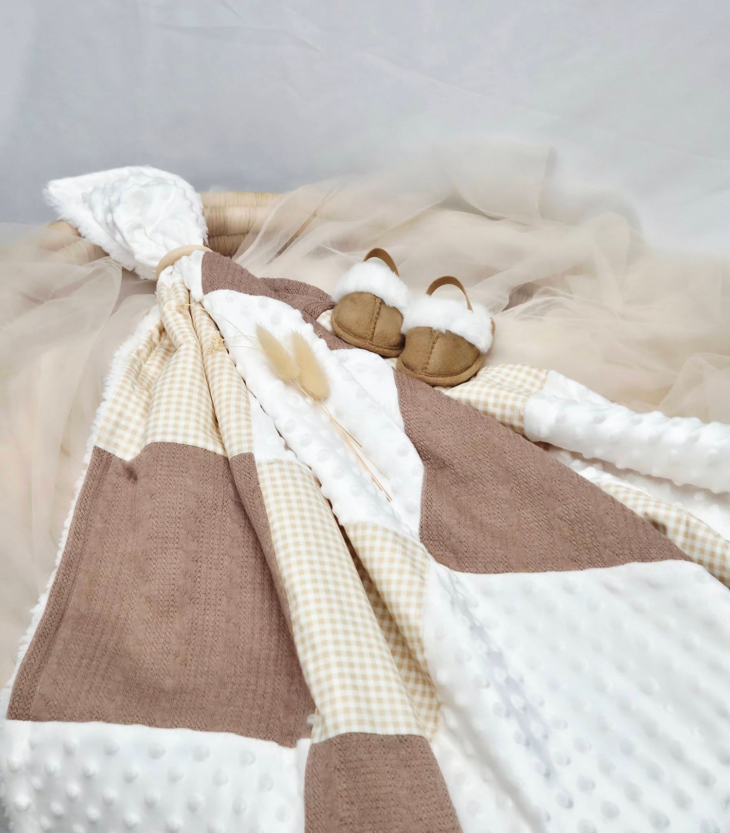 Neutral-toned baby gift set with patchwork blanket in beige, white, and brown gingham, paired with small brown shoes.