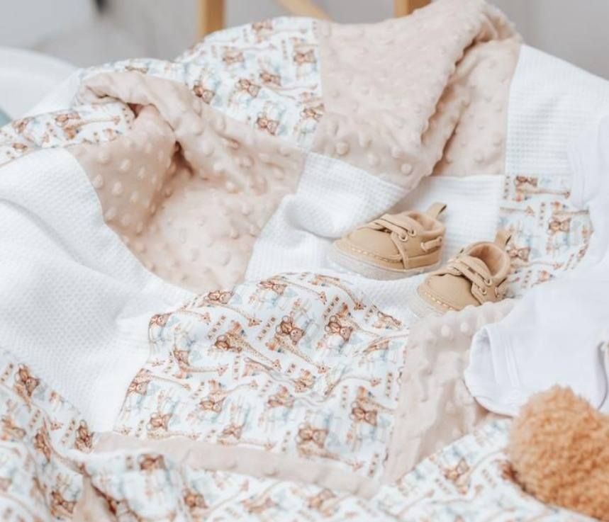 Soft baby blanket set with teddy bear print in neutral beige tones, paired with tiny booties on a white surface.