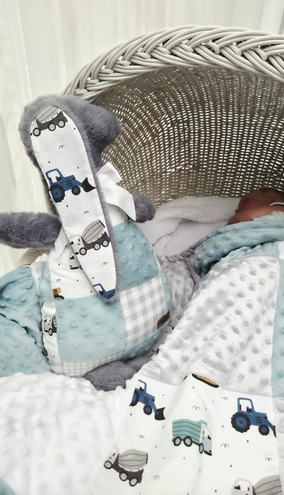 Baby boy nursery set with tractor print blanket, gray minky dot fabric, and stuffed bunny toy in a wicker Moses basket.