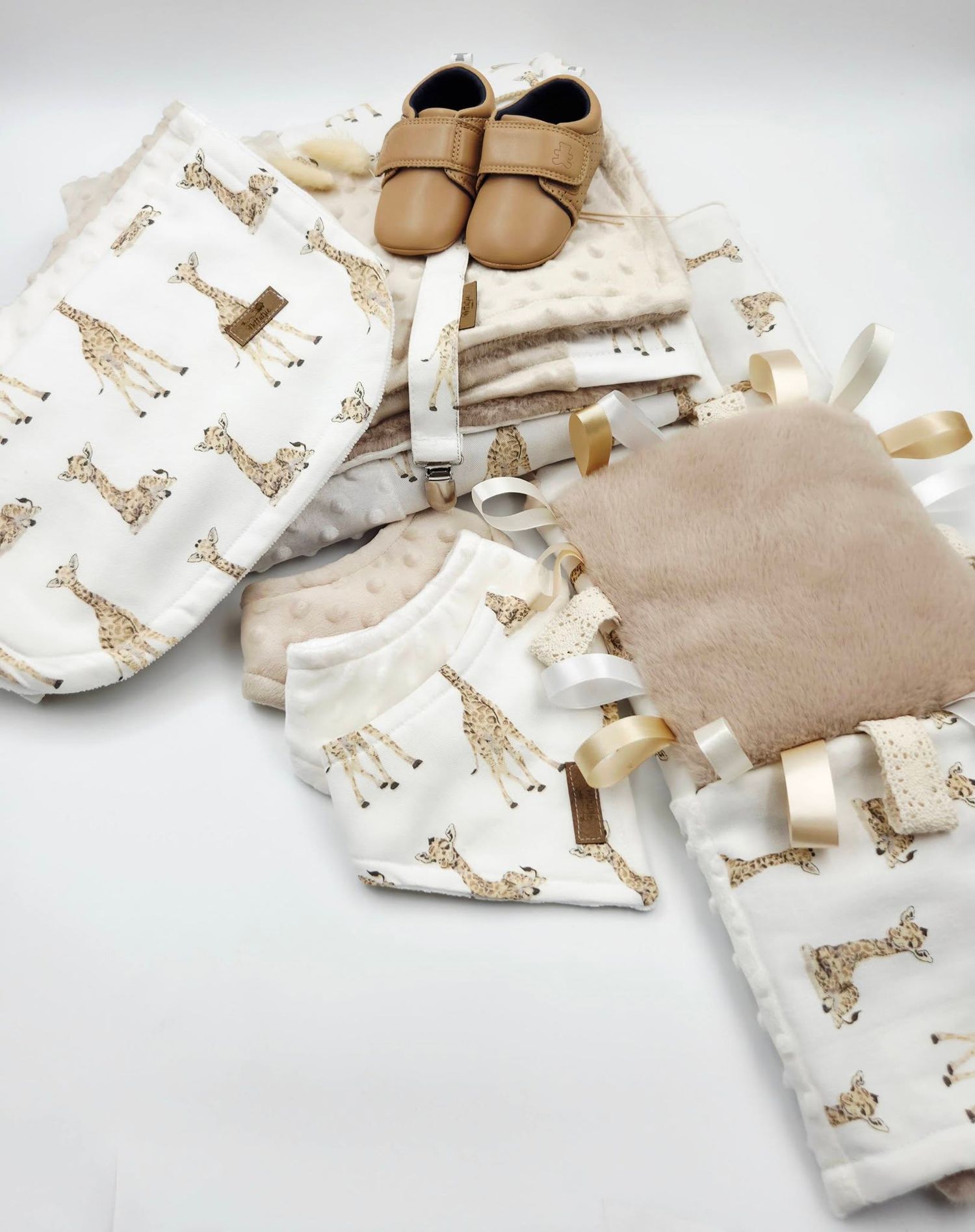 Giraffe print baby gift set with blanket, bib, tag toy, and tan leather moccasins on white background.