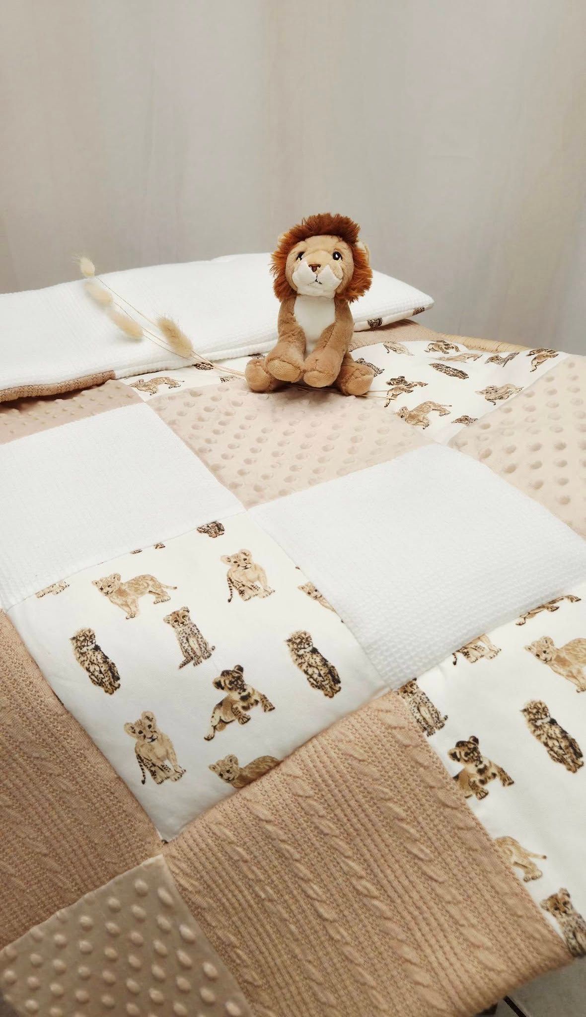 Handmade patchwork baby quilt in beige and white with safari animal print, styled with a plush lion stuffed toy.