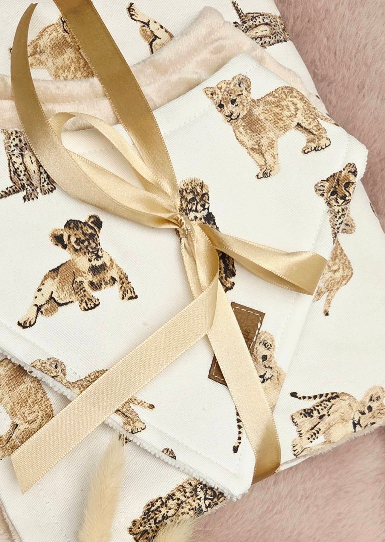 White gift wrap featuring illustrated baby lion cubs and cheetahs, tied with a satin gold ribbon bow.
