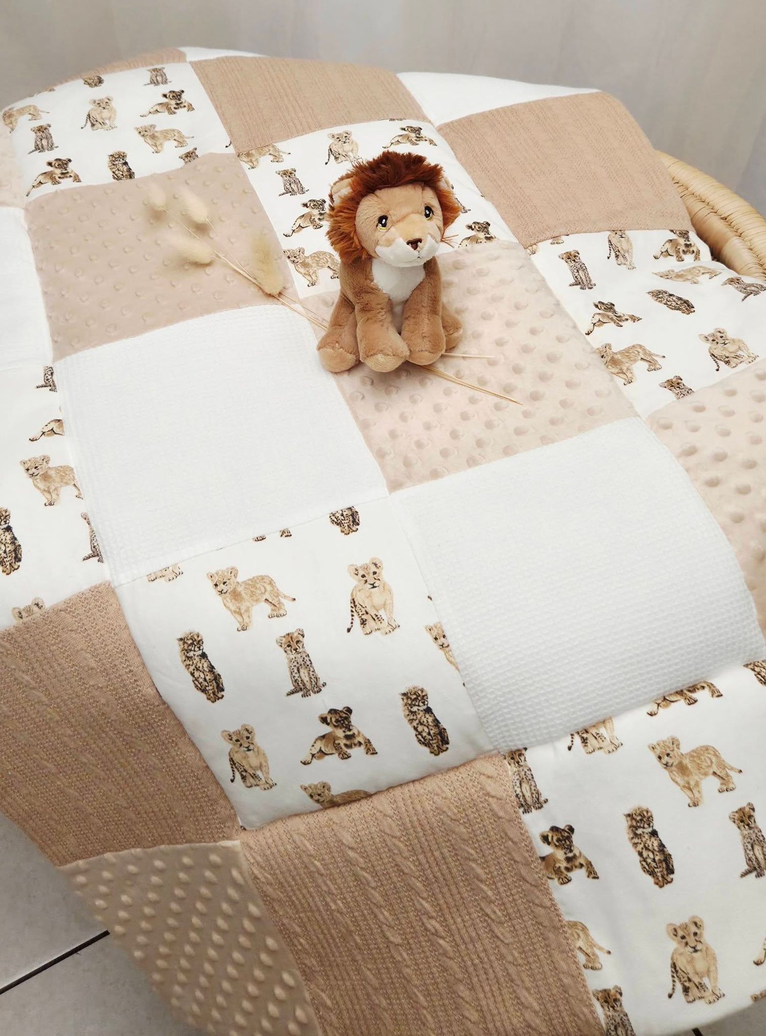 Beige patchwork baby quilt with safari animal print squares and a plush lion stuffed toy sitting on top.