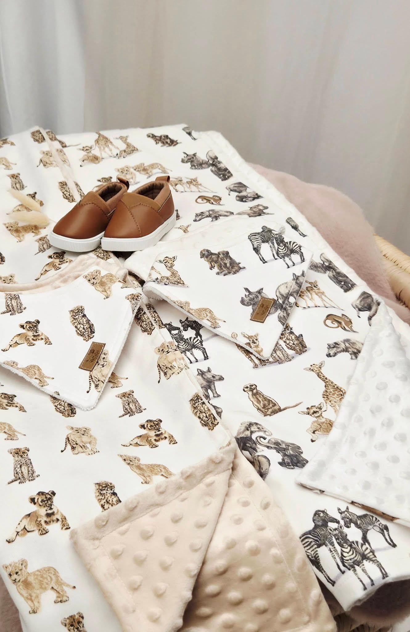 White animal print baby blanket set with minky dot fabric and brown leather baby shoes on a pink bed.