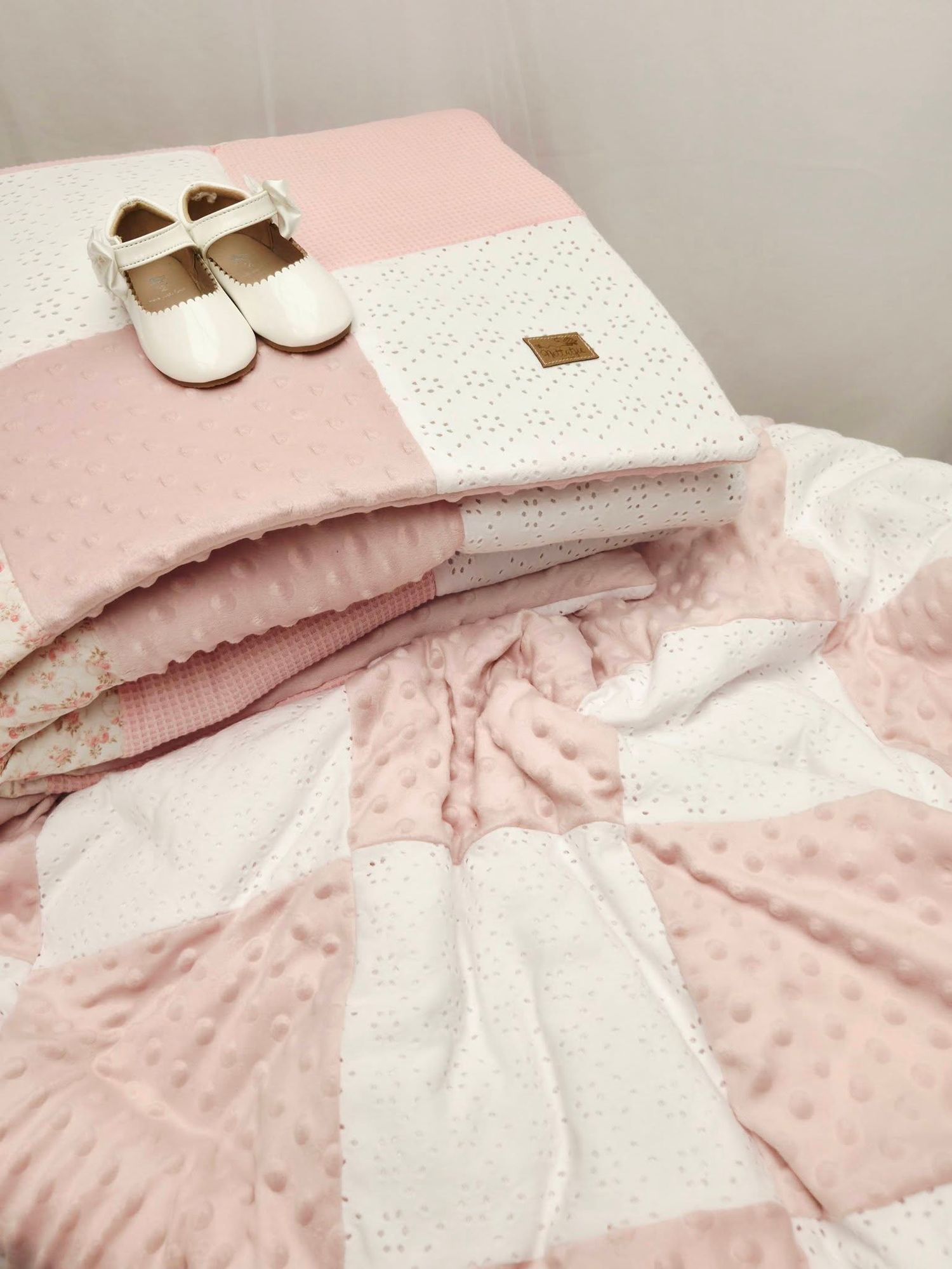 Pink and white baby patchwork blanket with minky dots, folded neatly with white baby shoes on top.