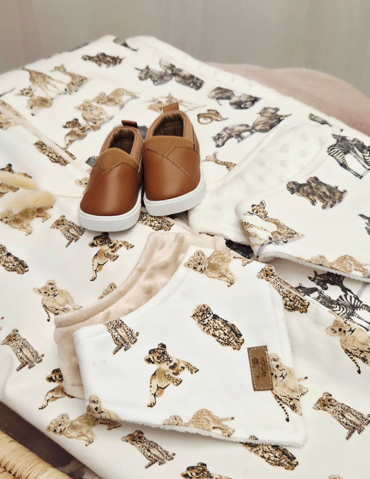 Baby safari animal print blanket and onesie set with brown leather slip-on shoes on a neutral background.