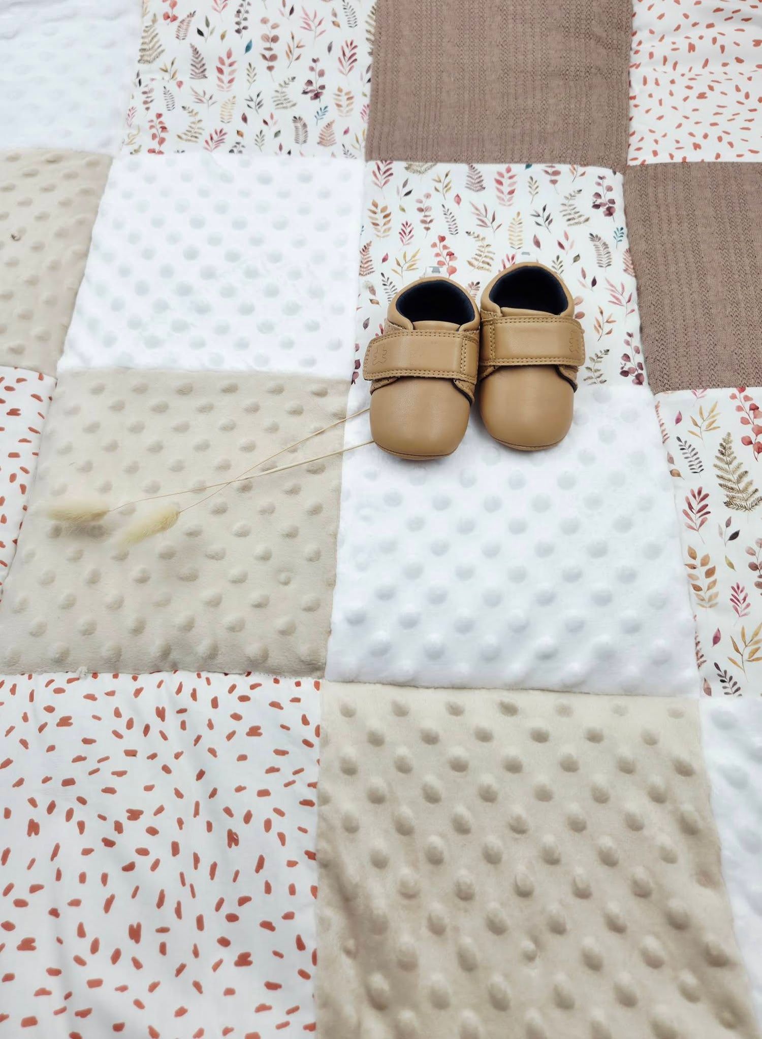 Patchwork baby play mat with floral and minky dot squares in neutral tones, with tan leather baby moccasins on top.