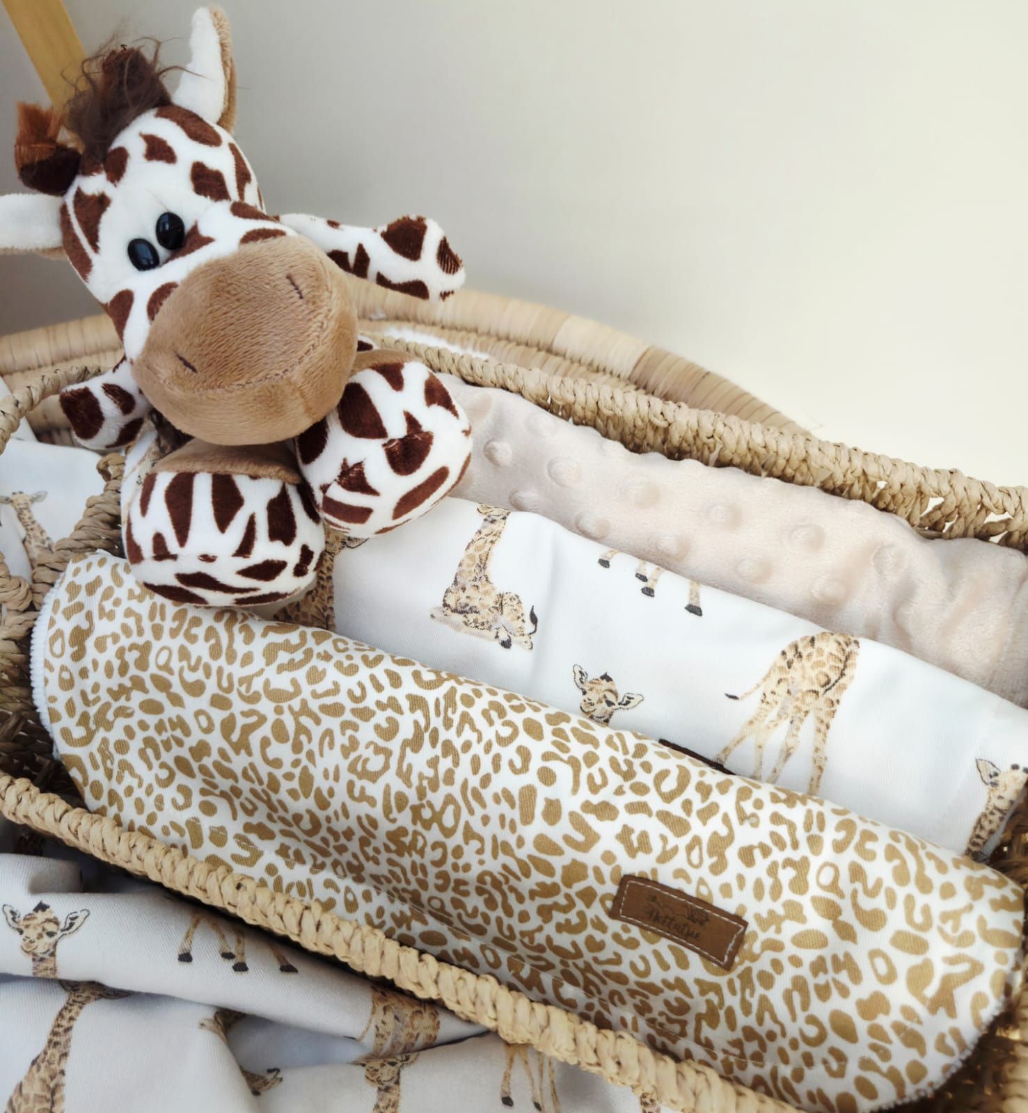 Plush giraffe toy resting on a beige and brown leopard print body pillow with matching bedding accessories.