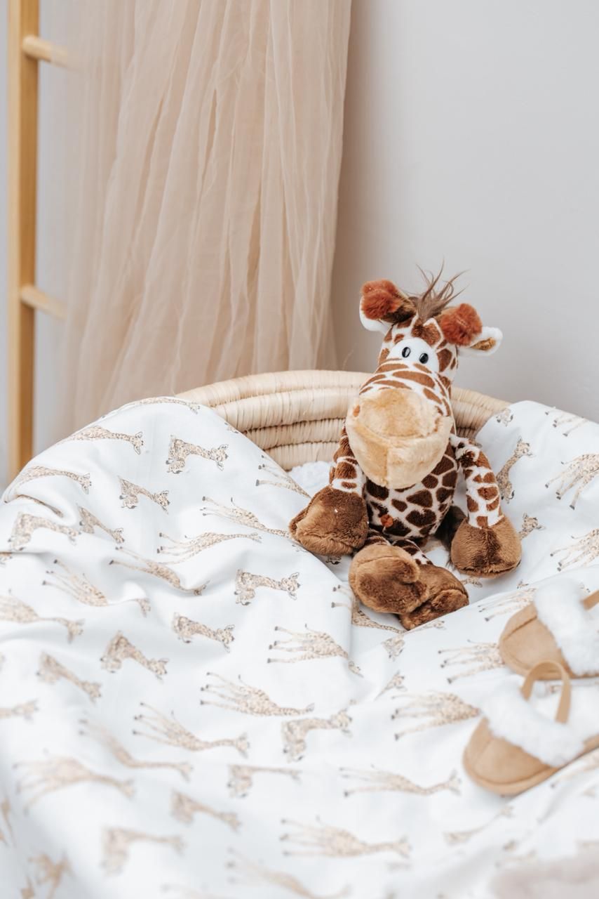 Plush giraffe toys peeking out from white patterned bedding.