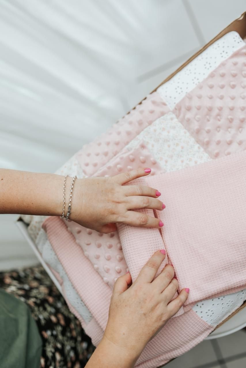 Hands gently folding and arranging soft pink and white textured fabric or bedding material.
