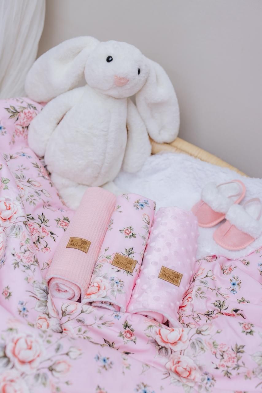 White plush bunny toys rest on pink floral bedding with delicate rose patterns and soft textures.