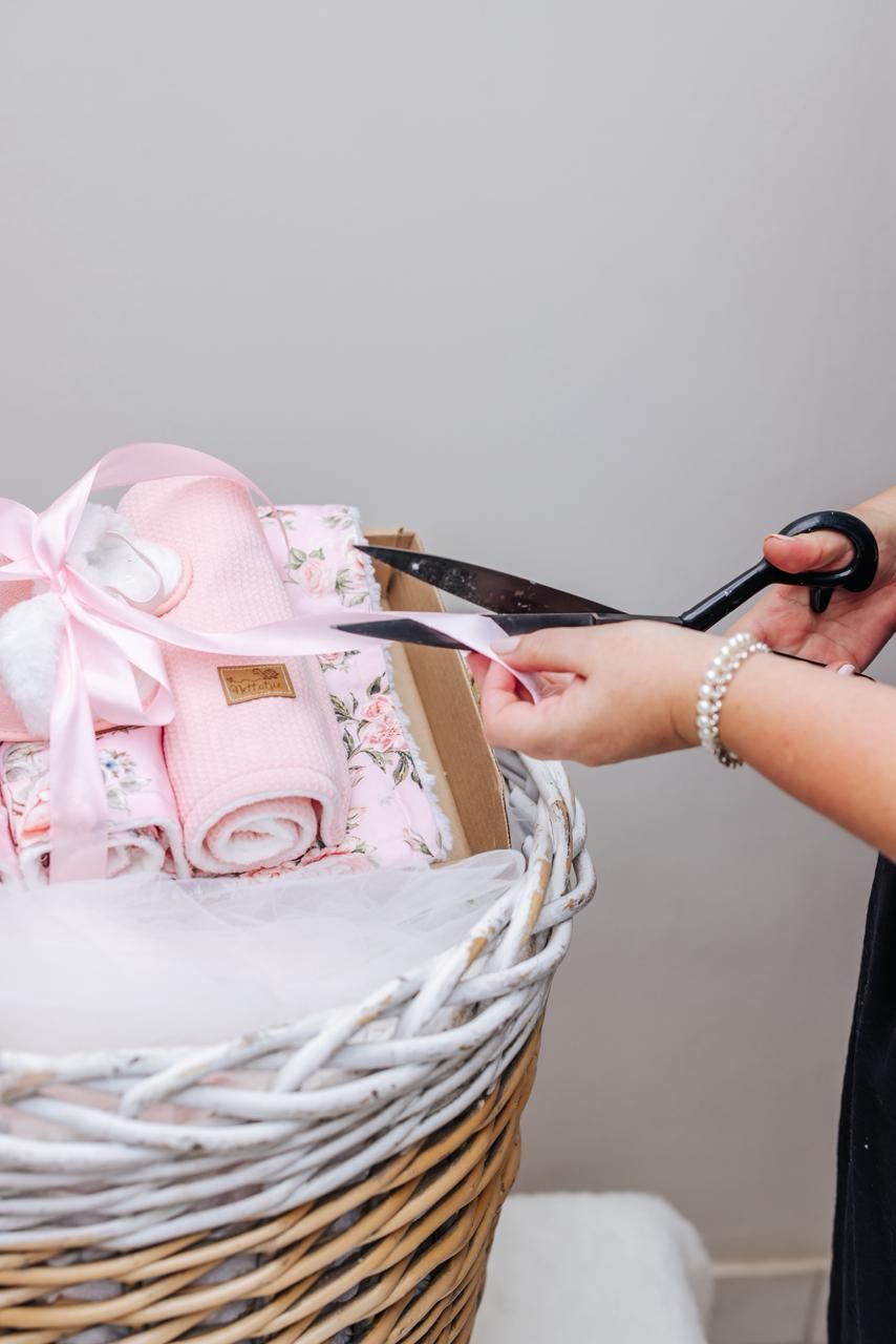 A person places folded pink and white fabric into a woven wicker laundry basket.