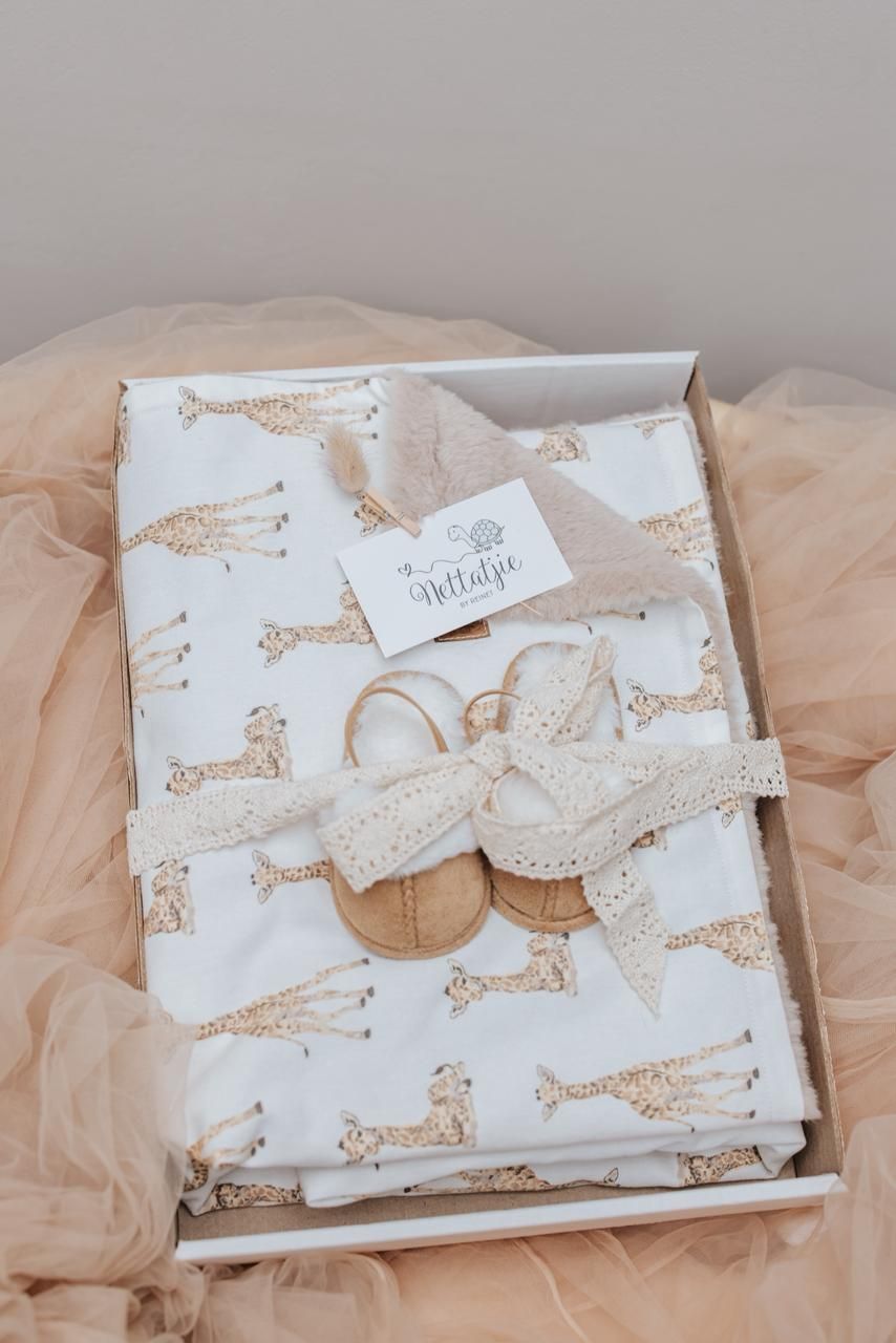 White baby swaddle blanket with giraffe print pattern neatly folded in a gift box with tulle fabric.