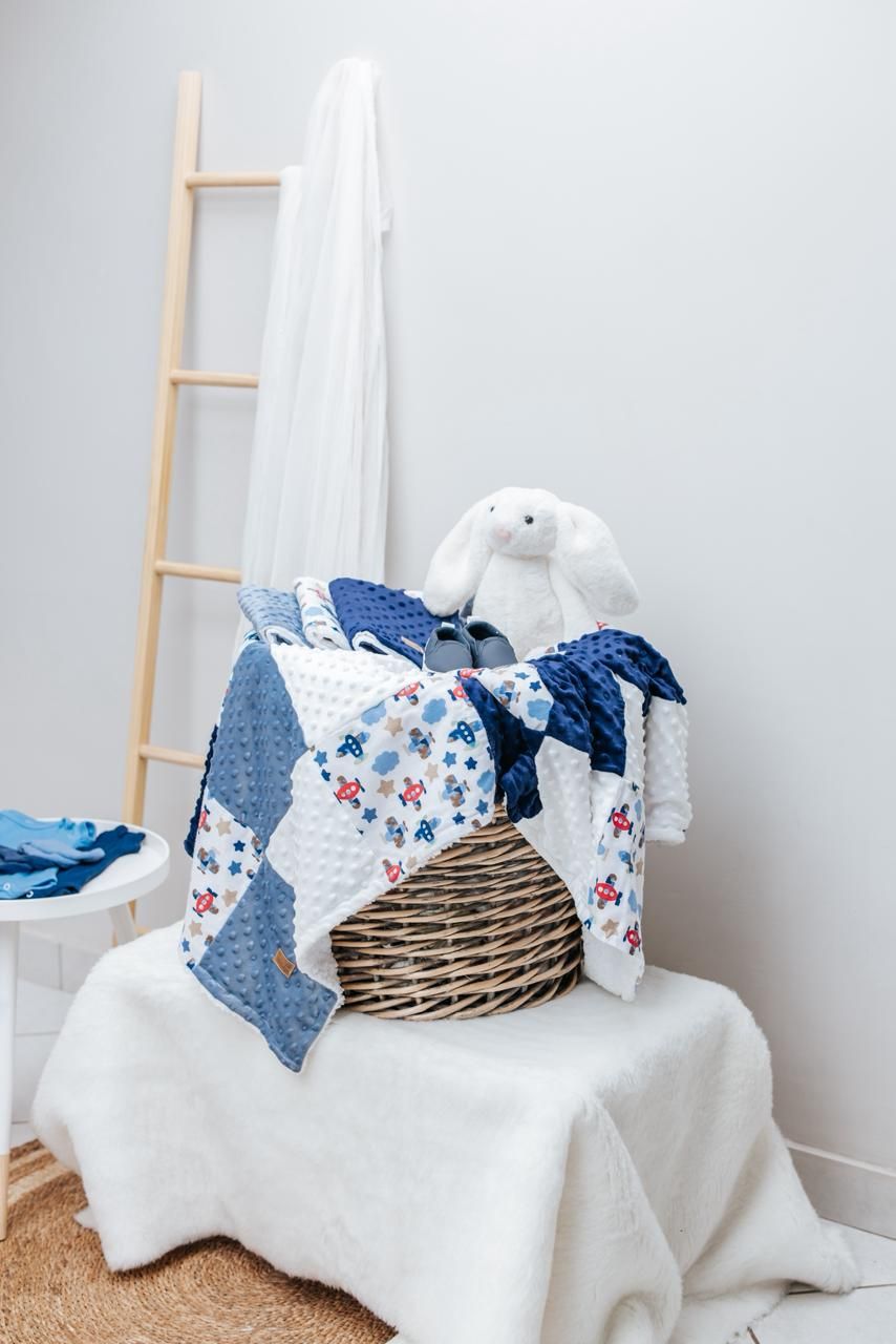 Blue and white floral baby bedding arranged in wicker basket with plush bunny.