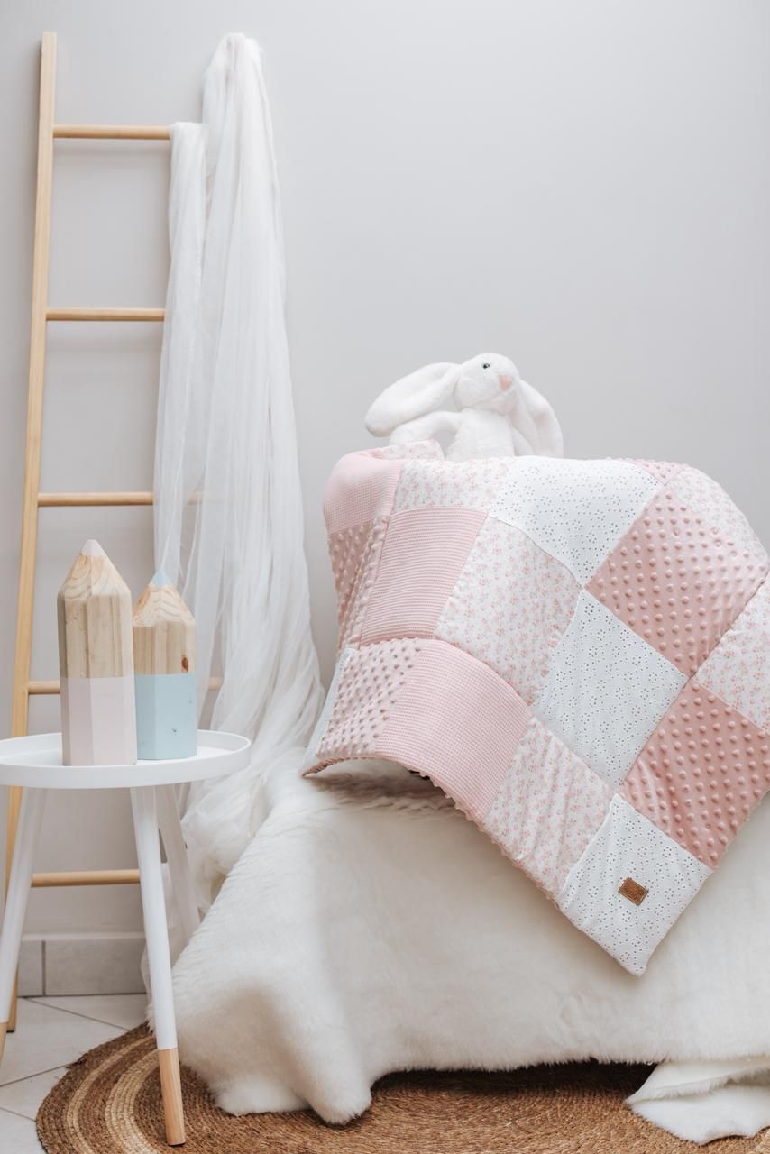 Cozy pink and white patchwork nursery decor with blankets, cushions and decorative ladder against light wall.