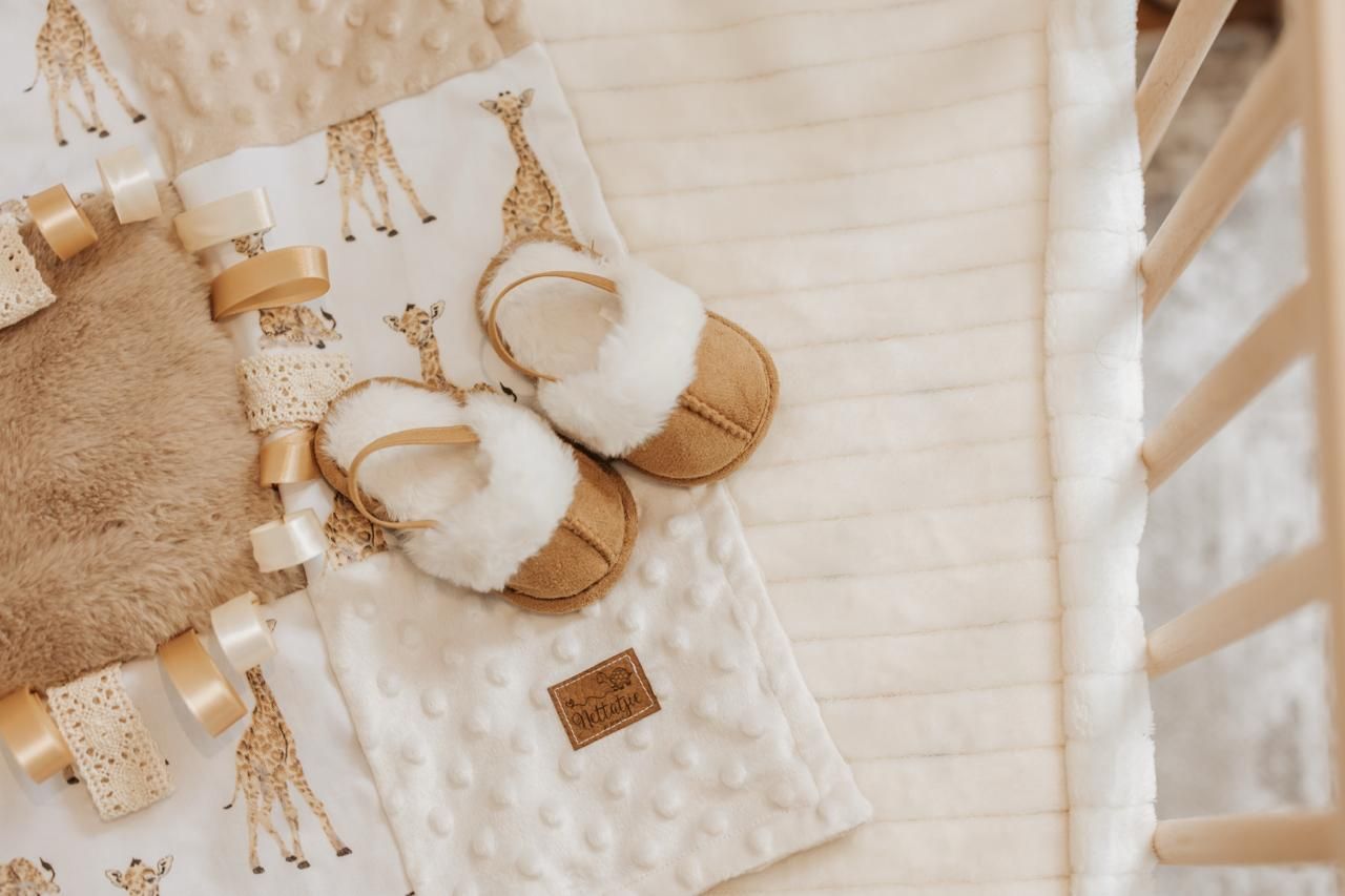 A collection of baby items including a stuffed giraffe, white booties, and soft blankets arranged in a neutral color palette.