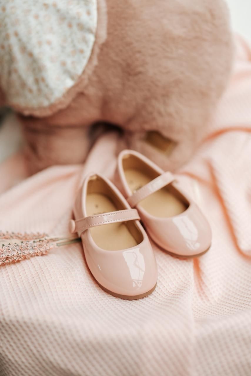 A pair of shiny pink patent leather Mary Jane shoes for toddlers displayed on soft pink fabric.