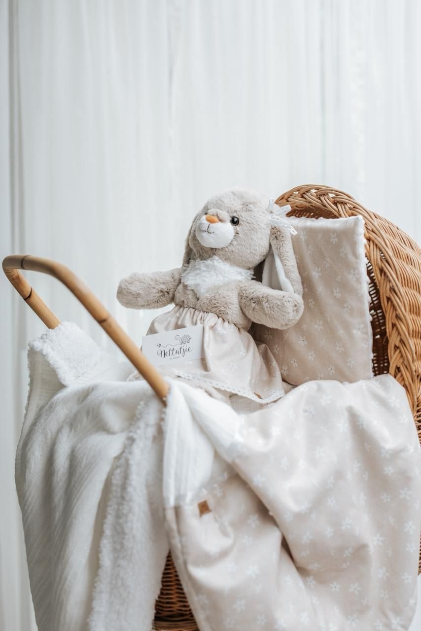 Soft plush bunny toy and white blankets arranged in wicker basket against white wall background.