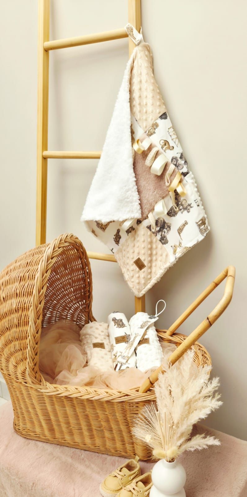 Woven basket with baby items, blanket, and pampas grass decor arranged in a cozy nursery corner with wooden ladder.