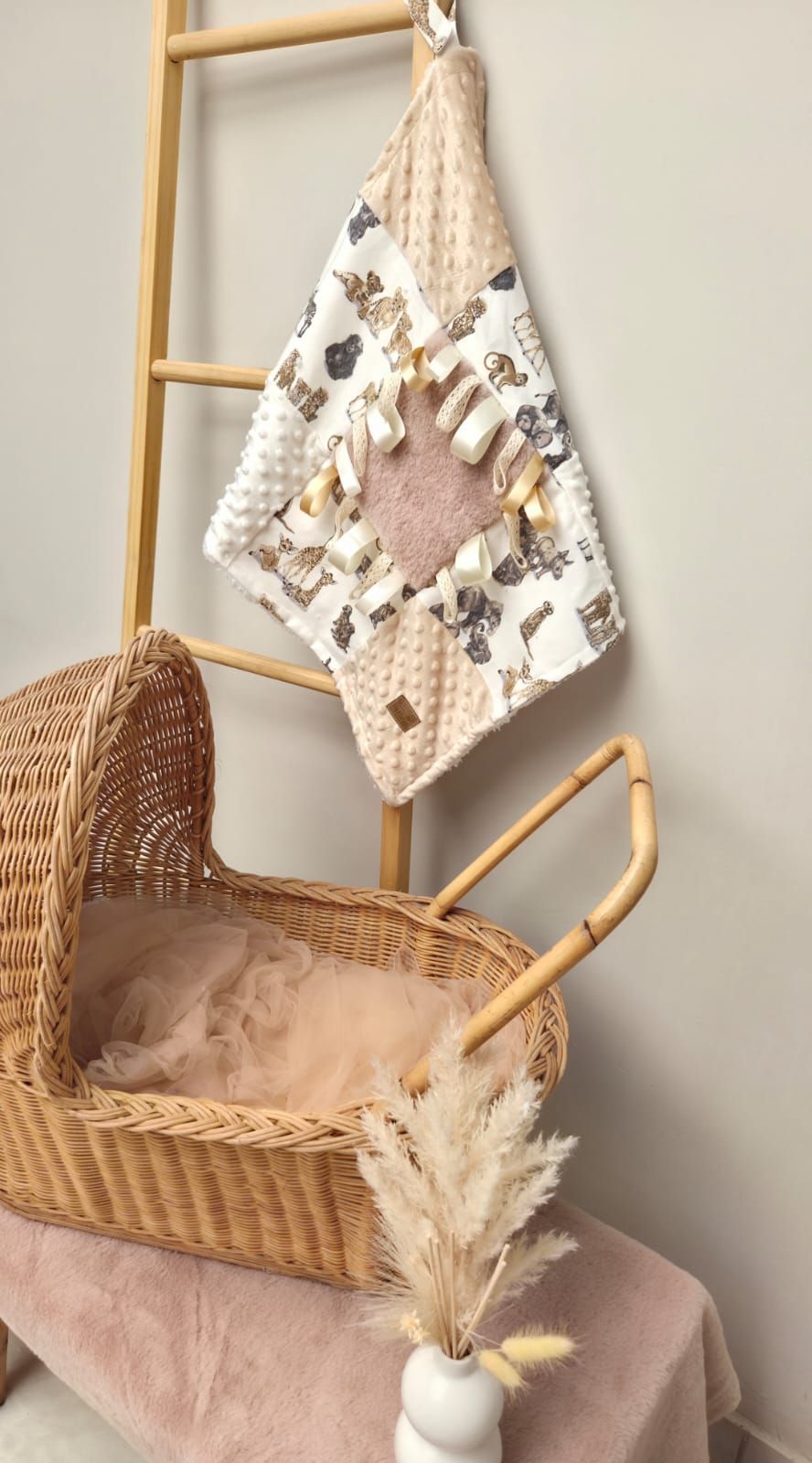 Cozy wicker baby bassinet with pink cushioning and decorative hanging towels in a nursery corner setting.