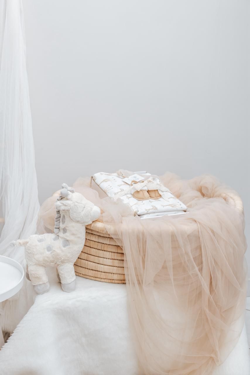 Soft beige tulle draped over woven basket with wrapped gifts and plush toy.