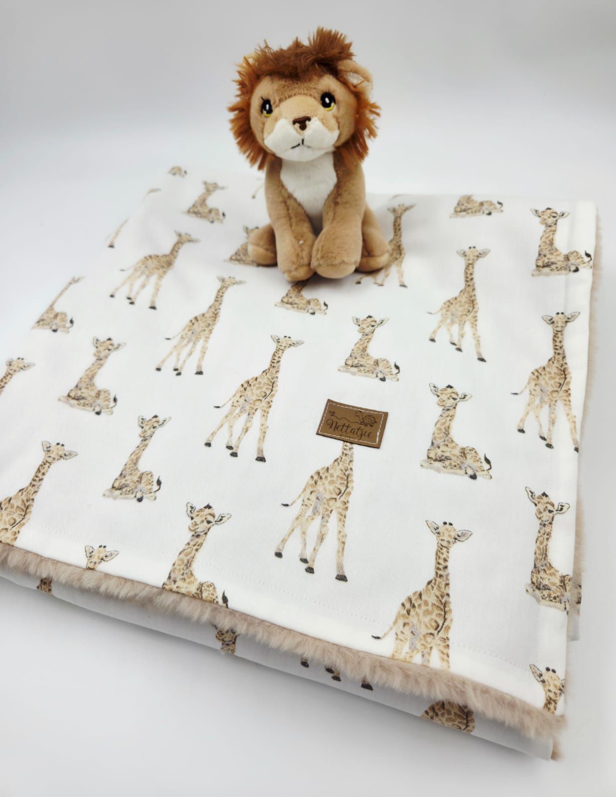 White fabric with repeating giraffe pattern design shown in multiple angles with plush lion toy accent.