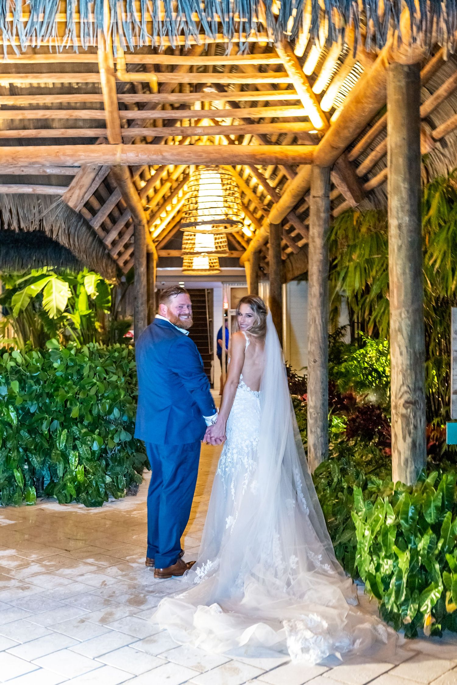 Wedding couple sharing a moment under a tropical wood-beamed pergola with lush greenery.