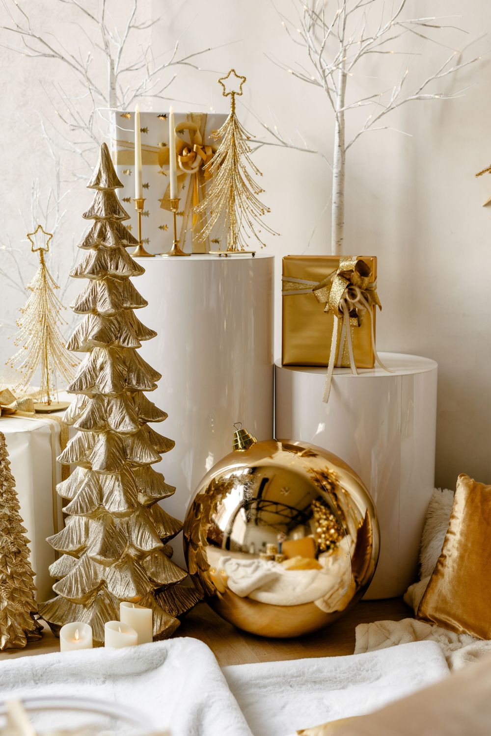 Gold and white Christmas decorations featuring metallic trees, large ornament ball, and tiered display stands.