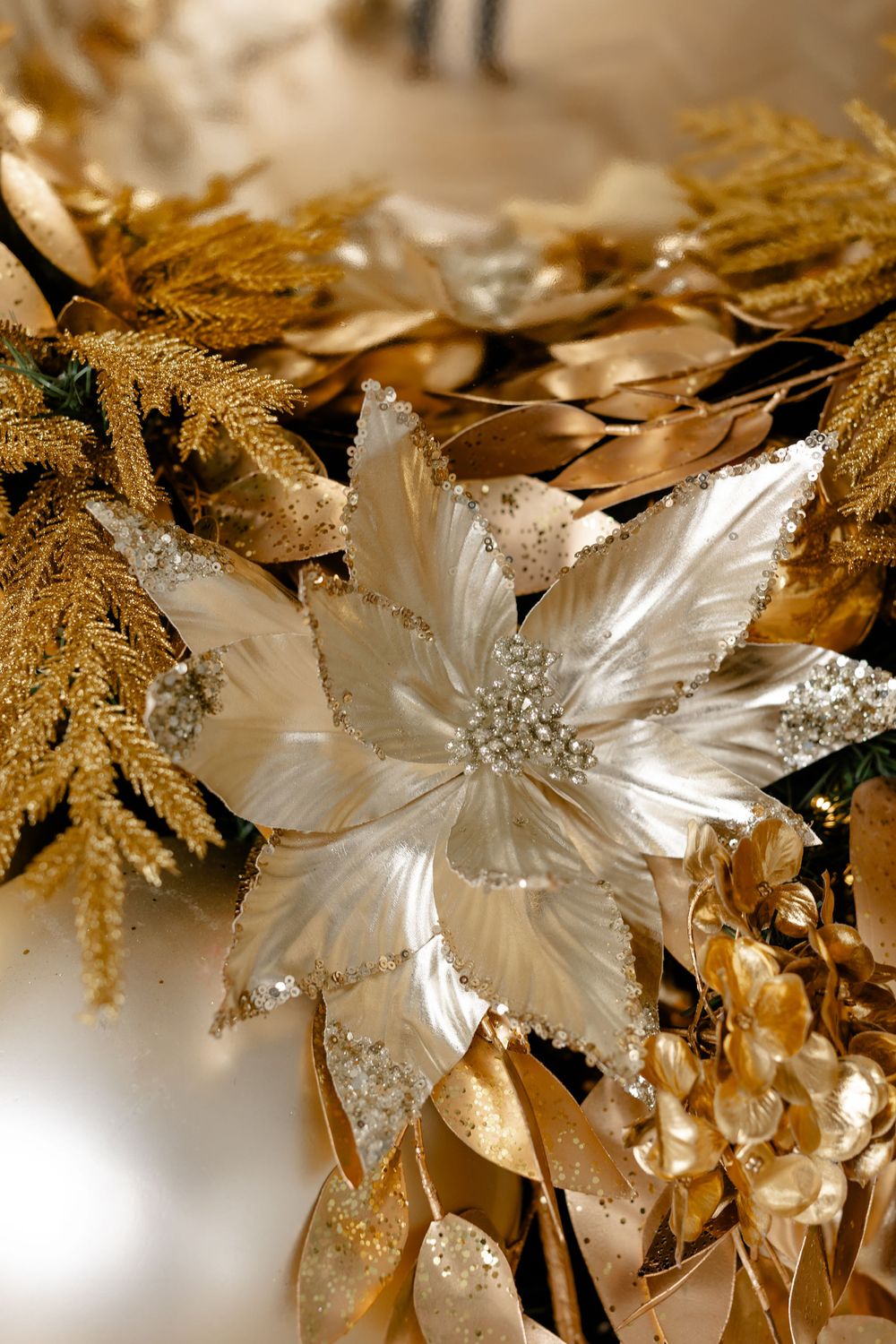 Close-up of glittery white poinsettia Christmas ornament with gold leaves and sparkly accents.