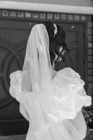 Black and white wedding photo showing back view of a bride with long delicate veil and flowing dark hair.