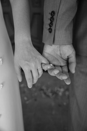 A closeup of hands showing engagement or wedding rings in black and white.