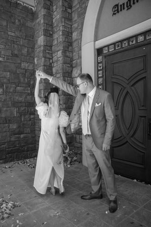 Black and white photo of a couple dancing together outside a grand doorway with stone brick walls and ornate entrance.