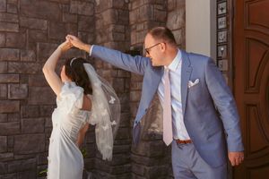 A couple in wedding attire share a romantic dance moment against a rustic brick wall backdrop.