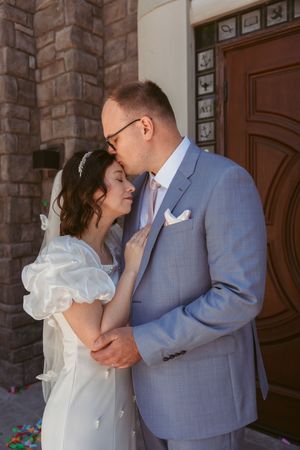 Newlywed couple shares intimate moment in front of ornate wooden door at brick church entrance.