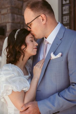 A tender wedding moment captured as newlyweds share an intimate embrace, with the bride in white and groom in light blue suit.