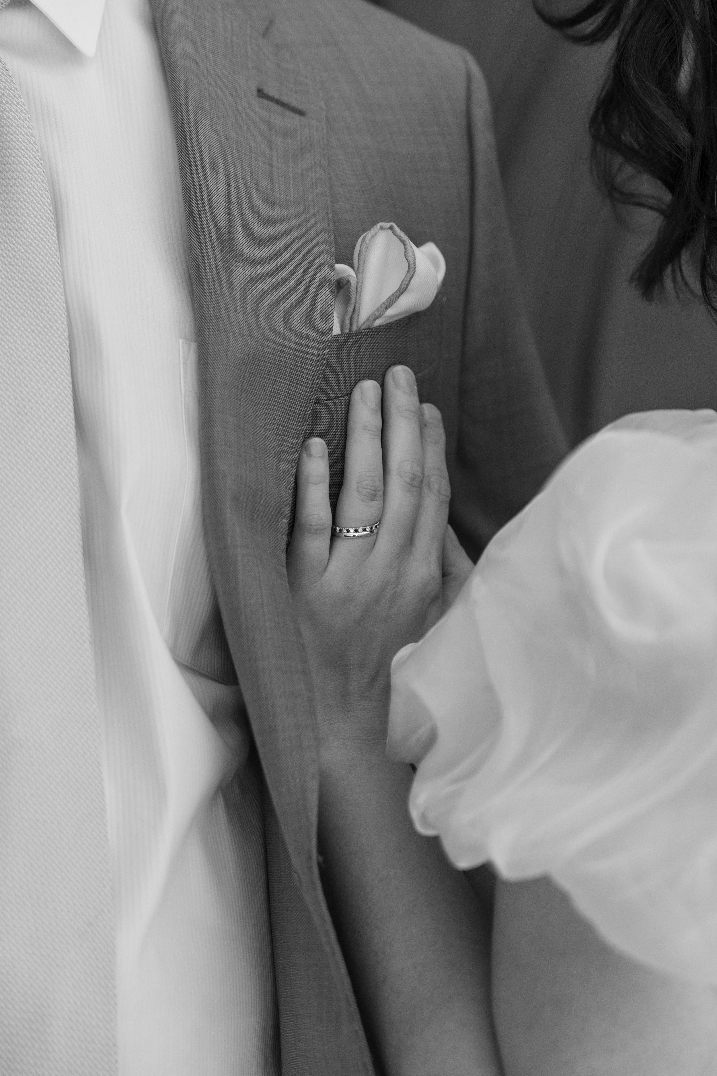 Close up black and white photo of hands and torso at a wedding with pocket square detail.