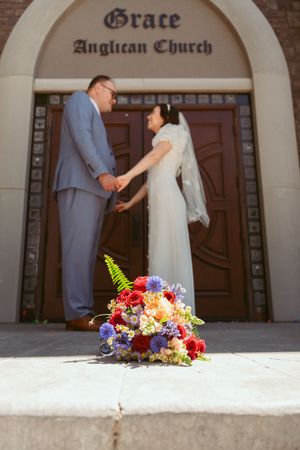 A colorful floral bouquet rests near Grace Anglican Church's wooden doors with rose petals scattered on the ground.