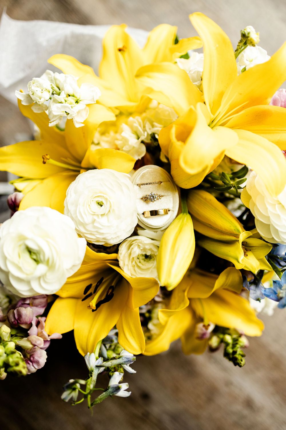 Beautiful wedding bouquet featuring bright yellow lilies and white ranunculus flowers arranged with greenery.
