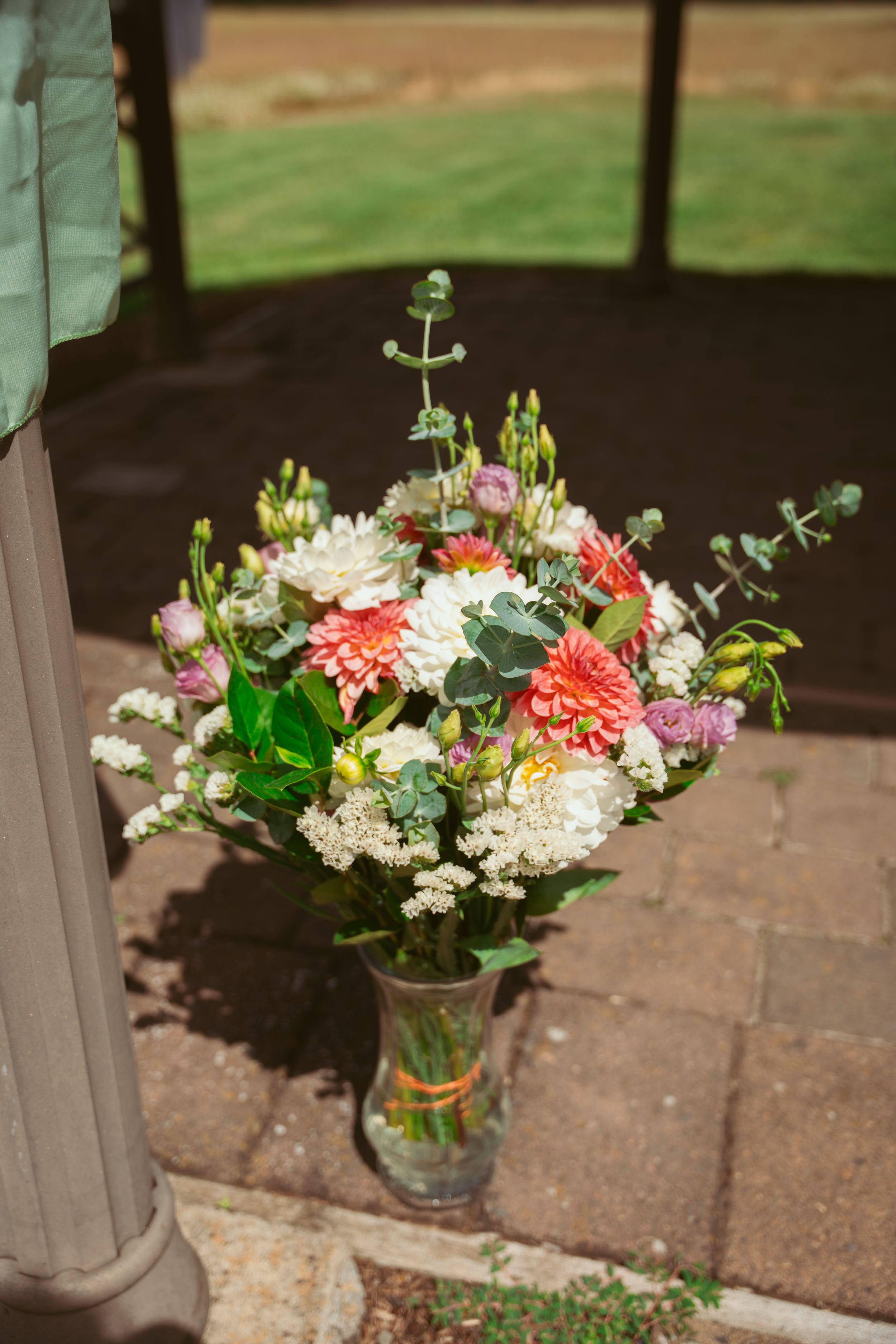 A mason jar filled with colorful seasonal flowers including coral dahlias and white blooms sits on outdoor brick steps.